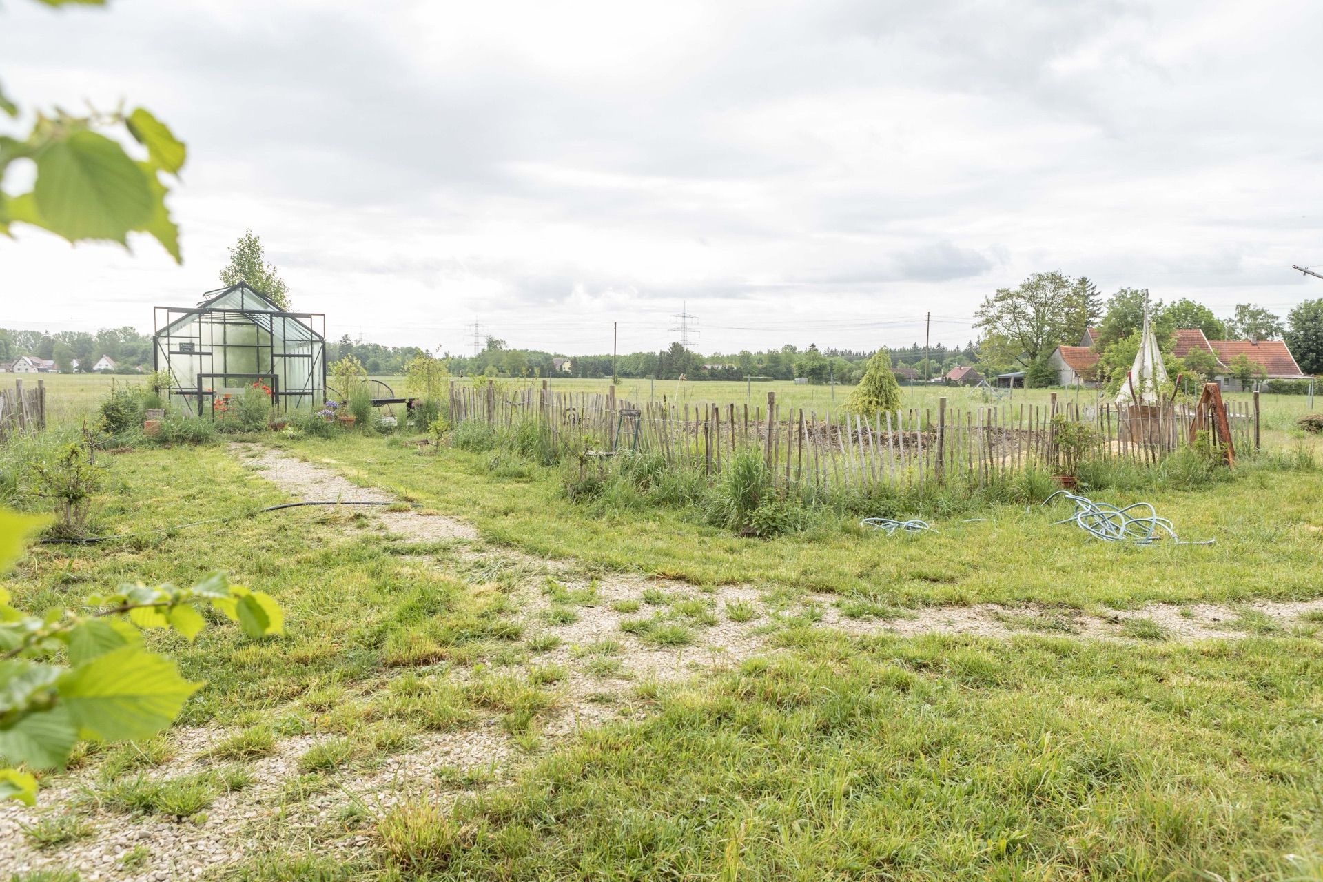 Weite Blumenwiese mit dem schwarzen Gewächshaus und Blick über die Felder