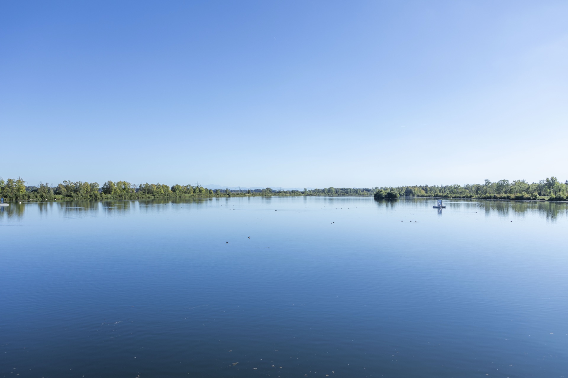 Weite, stille Seefläche mit flachem Ufersaum am Horizont