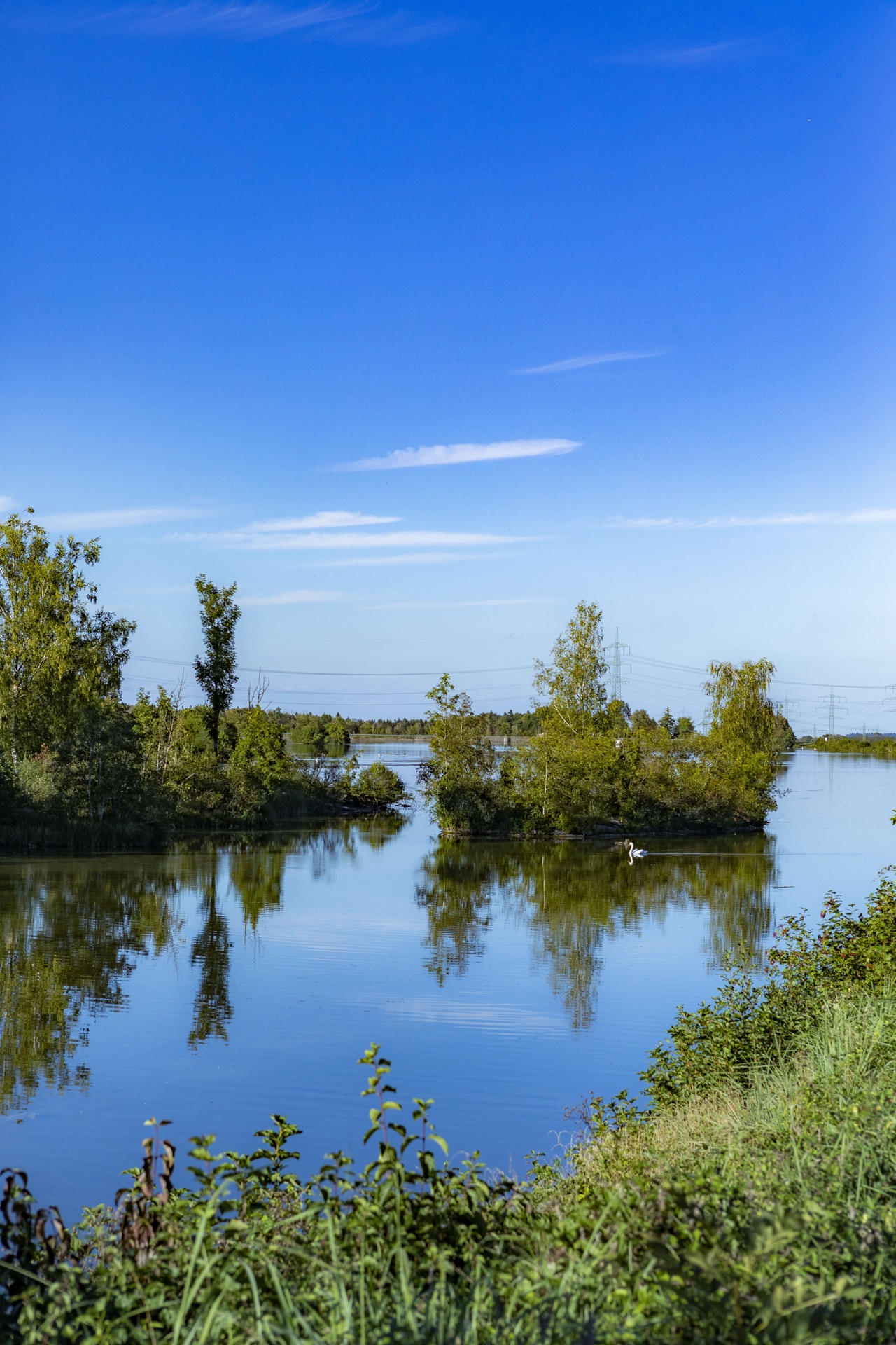 Kleine bewachsene Inseln spiegeln sich in einem See unter tiefblauem Himmel