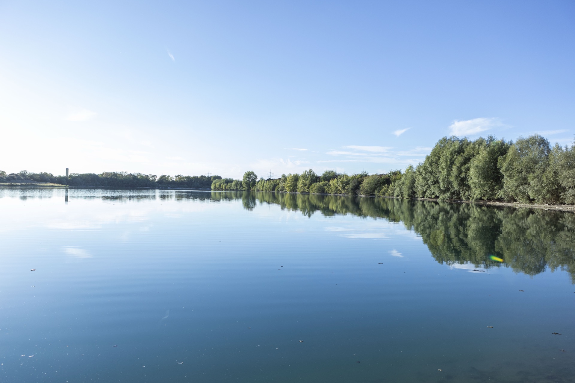 Spiegelglatter See mit bewaldetem Ufer unter blauem Himmel